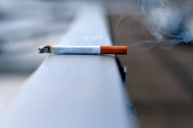 A smoking cigarette sitting on a fence rail.