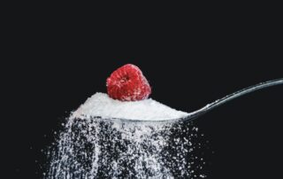 A tablespoon of white table sugar topped with a red raspberry.
