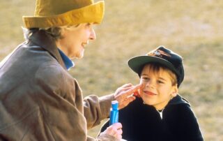 A grandmother applies sunscreen to her grandson's smiling face.