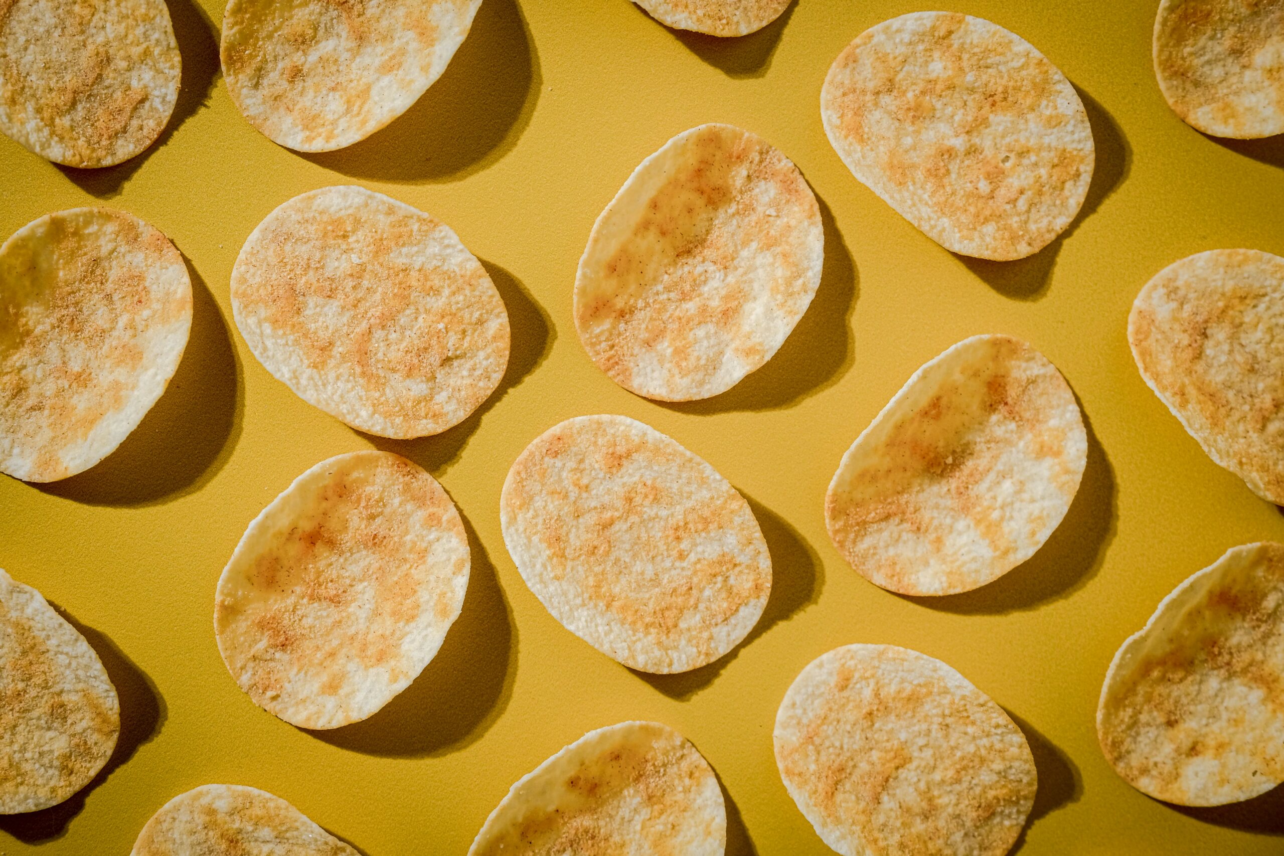 An array of artificially flavored potato chips on a yellow background.